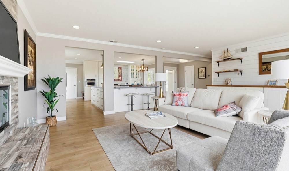 Staged coastal living room with white sofa, fireplace, and breakfast bar