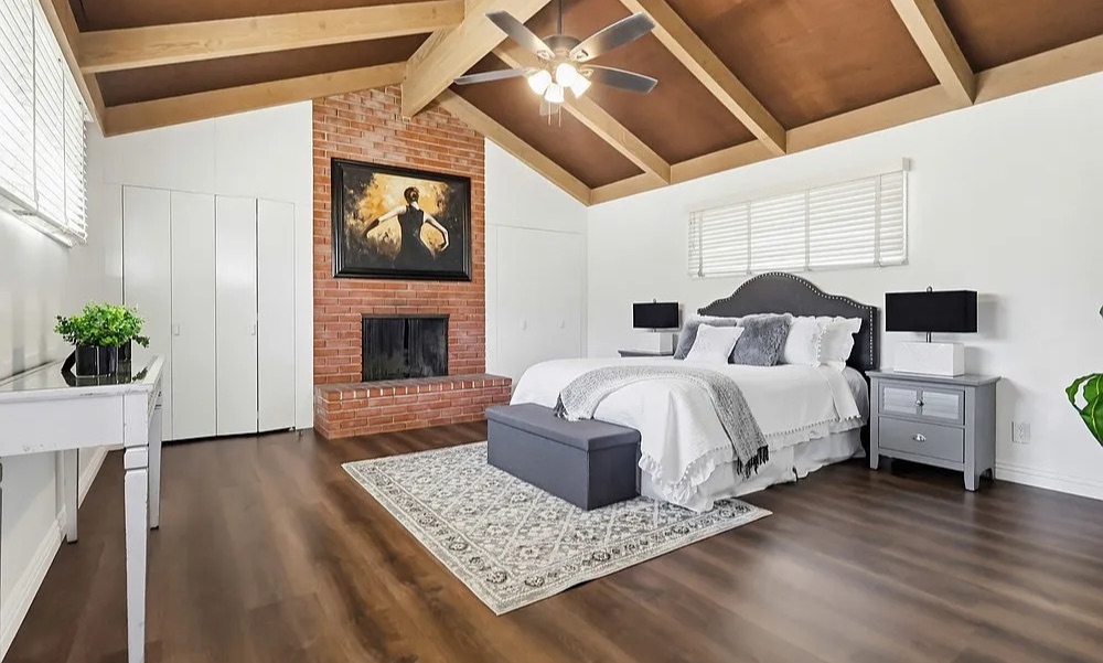 Staged primary bedroom with brick fireplace and vaulted wood-beam ceiling